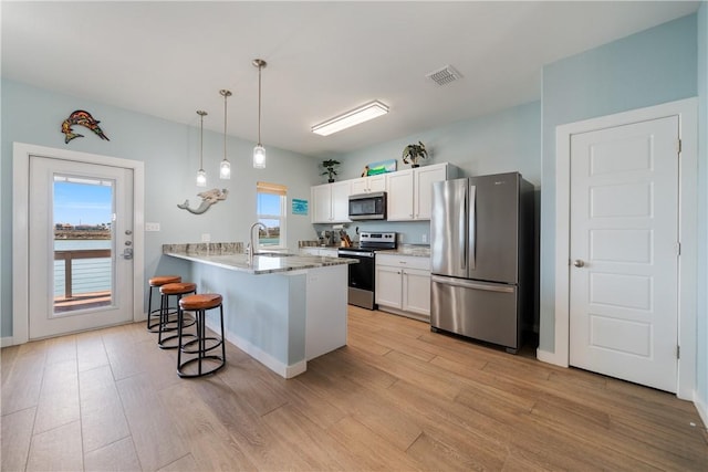 kitchen featuring a kitchen bar, a peninsula, stainless steel appliances, white cabinetry, and a sink