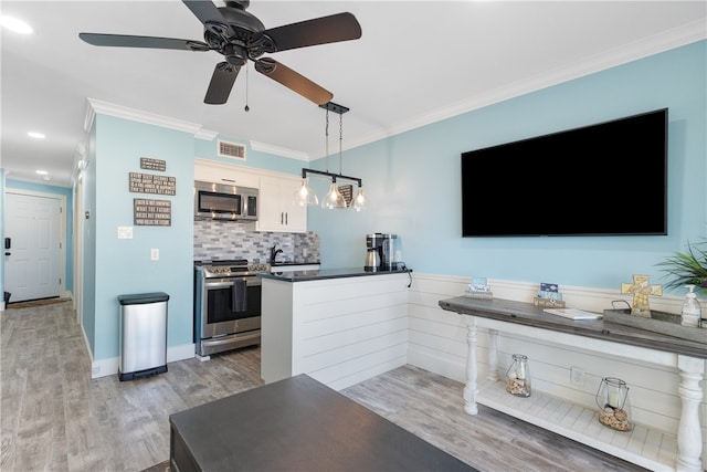 kitchen with light hardwood / wood-style floors, white cabinetry, appliances with stainless steel finishes, ornamental molding, and pendant lighting