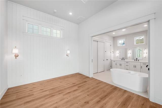 bathroom with a washtub, wood-type flooring, sink, and wooden walls