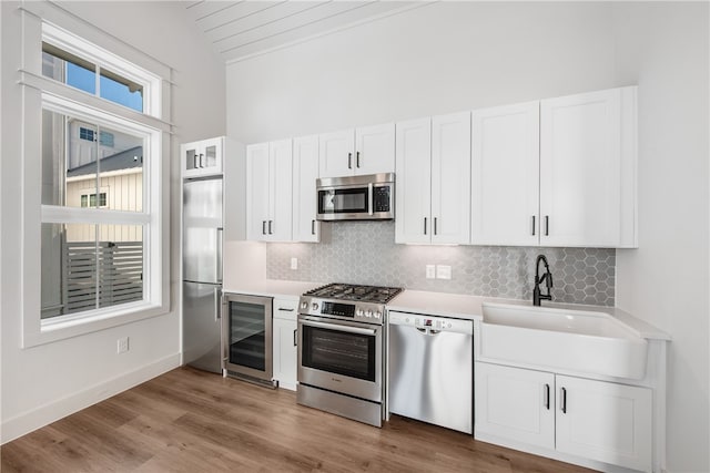 kitchen with stainless steel appliances, vaulted ceiling, white cabinets, sink, and wine cooler