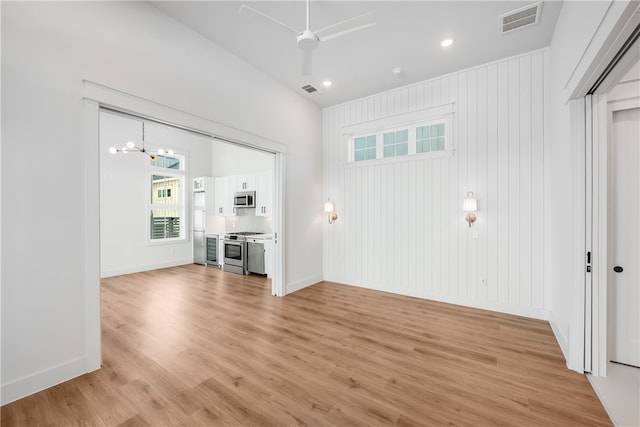 unfurnished living room featuring light hardwood / wood-style floors, wooden walls, and an inviting chandelier