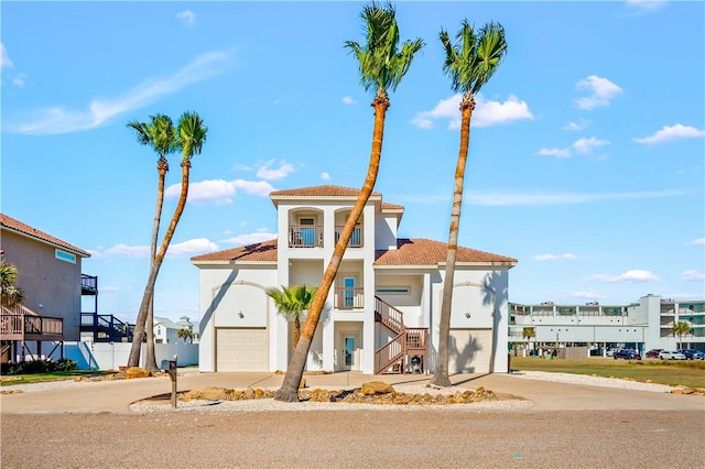 view of front of house with a balcony, a garage, a tile roof, stairs, and stucco siding