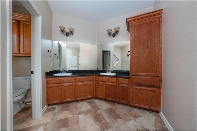 bathroom featuring baseboards, a sink, toilet, and double vanity