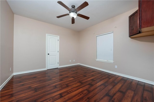 spare room featuring dark wood-style flooring, a ceiling fan, and baseboards