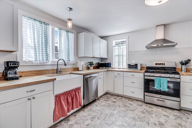 kitchen with white cabinetry, sink, appliances with stainless steel finishes, decorative light fixtures, and wall chimney range hood