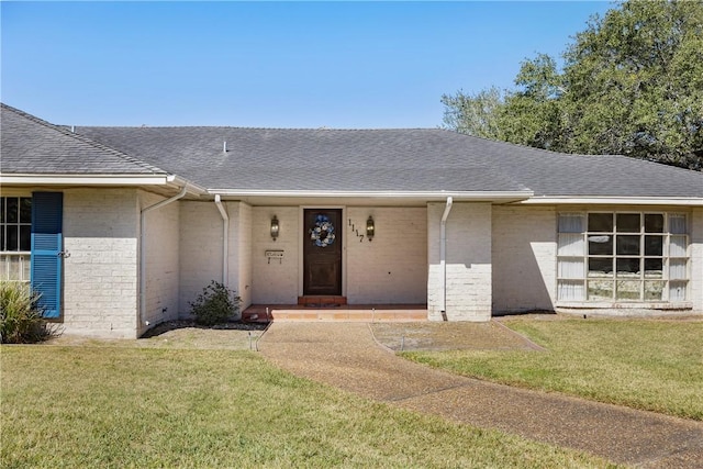 view of front facade with brick siding, a front lawn, and roof with shingles