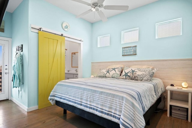 bedroom with a barn door, ensuite bath, hardwood / wood-style floors, and baseboards