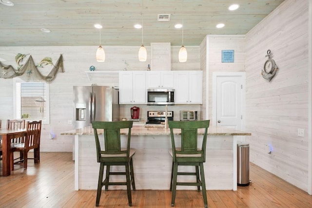 kitchen with light wood finished floors, appliances with stainless steel finishes, a kitchen bar, and light stone countertops