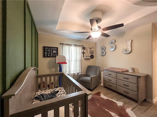 bedroom with a tray ceiling, a nursery area, and ceiling fan