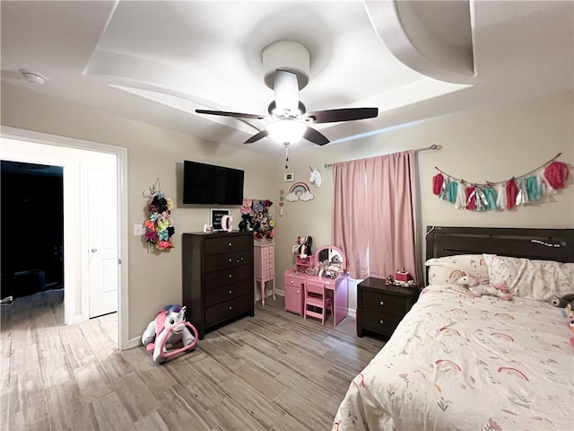 bedroom with ceiling fan, a raised ceiling, and light wood-type flooring