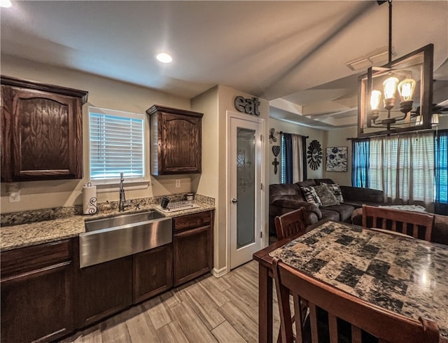 kitchen featuring light stone counters, dark brown cabinetry, sink, pendant lighting, and light hardwood / wood-style flooring