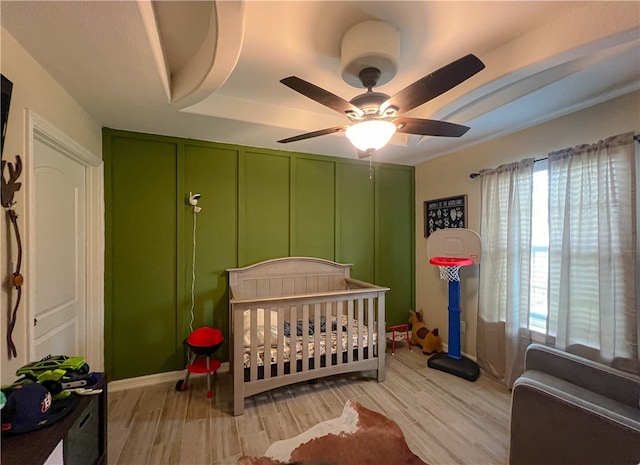 bedroom with light hardwood / wood-style floors, a nursery area, and ceiling fan