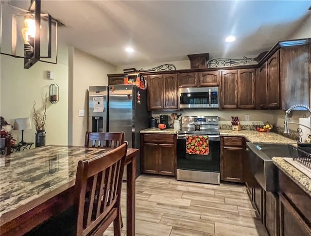 kitchen with stainless steel appliances, light hardwood / wood-style floors, dark brown cabinetry, light stone counters, and lofted ceiling