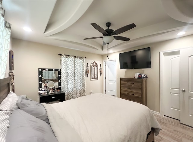 bedroom featuring ceiling fan, light wood-type flooring, and a tray ceiling