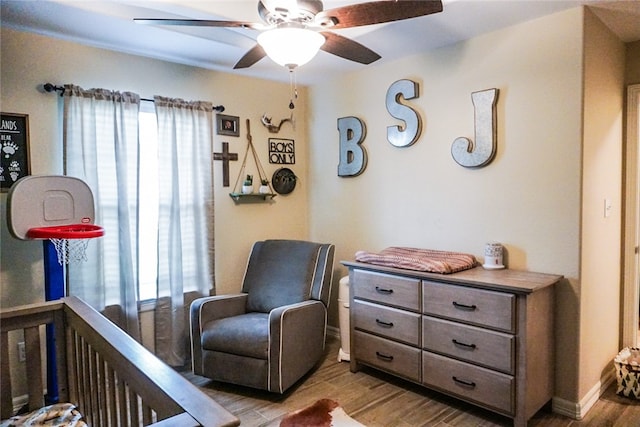 bedroom with multiple windows, wood-type flooring, ceiling fan, and a crib