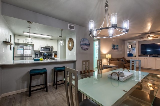 dining room with sink, ceiling fan with notable chandelier, and wood-type flooring