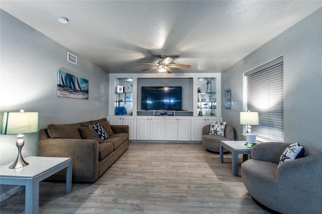 living room featuring ceiling fan, a textured ceiling, built in features, and light hardwood / wood-style floors