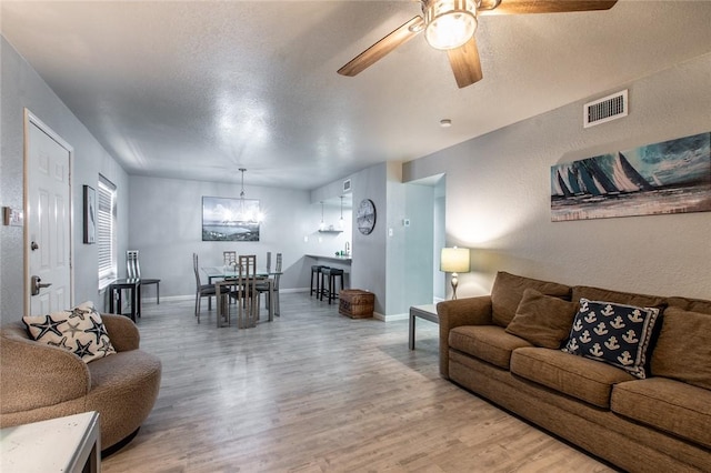 living room with ceiling fan with notable chandelier, hardwood / wood-style flooring, and a textured ceiling