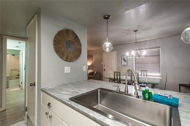 kitchen with light tile patterned floors, a notable chandelier, pendant lighting, white cabinets, and sink