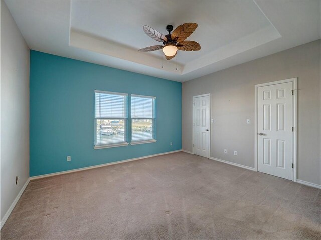 carpeted empty room with baseboards, a raised ceiling, and a ceiling fan