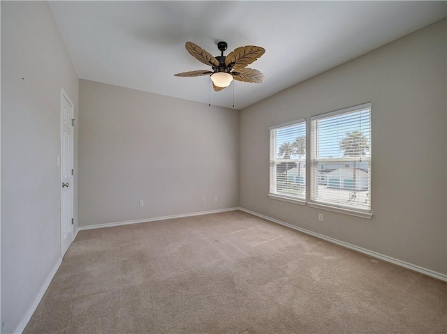 spare room featuring light carpet, a ceiling fan, and baseboards