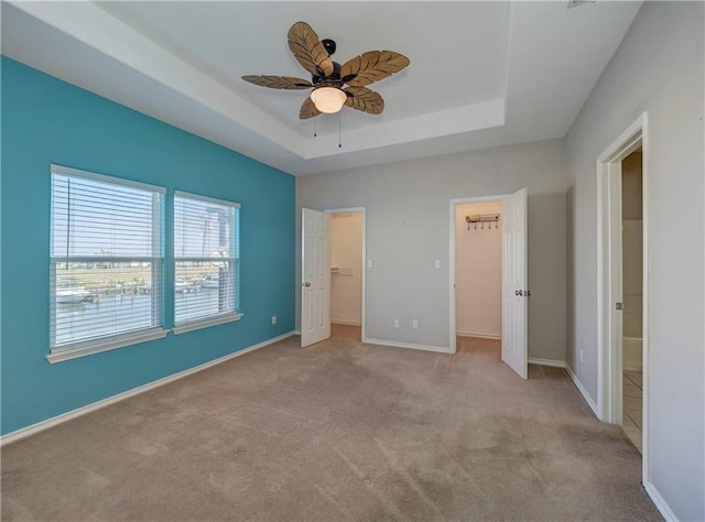 unfurnished bedroom with baseboards, a tray ceiling, and a walk in closet