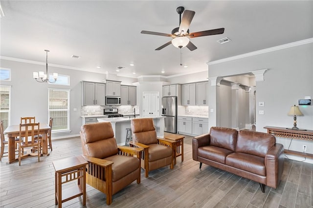 living room with visible vents, crown molding, light wood-type flooring, baseboards, and ceiling fan with notable chandelier