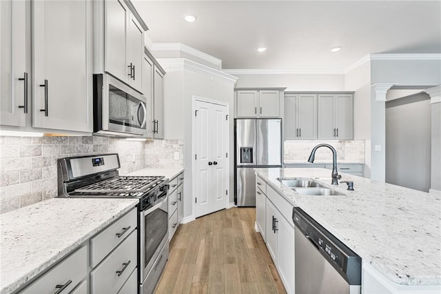 kitchen featuring light wood-type flooring, a sink, light stone counters, ornamental molding, and stainless steel appliances