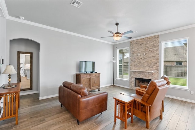 living room featuring a ceiling fan, visible vents, baseboards, ornamental molding, and light wood-style flooring