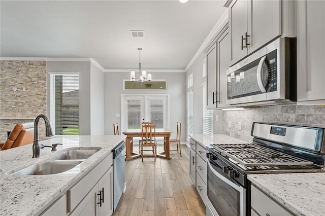 kitchen with light wood-type flooring, a sink, a notable chandelier, ornamental molding, and stainless steel appliances