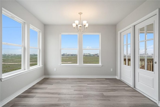 unfurnished dining area with a notable chandelier, baseboards, and wood finished floors