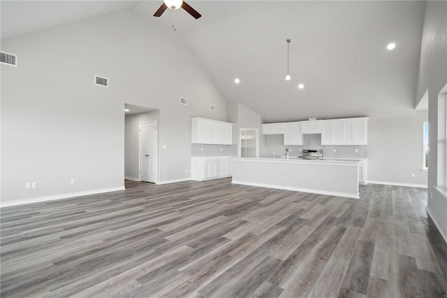 unfurnished living room featuring a ceiling fan, wood finished floors, visible vents, baseboards, and a sink