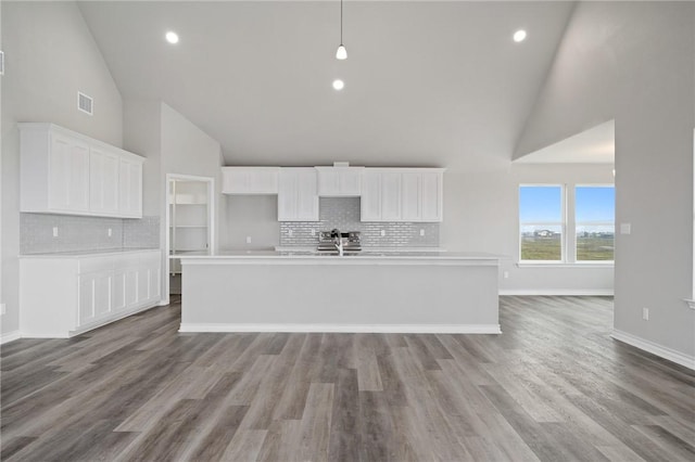 kitchen with a center island with sink, white cabinets, visible vents, and high vaulted ceiling