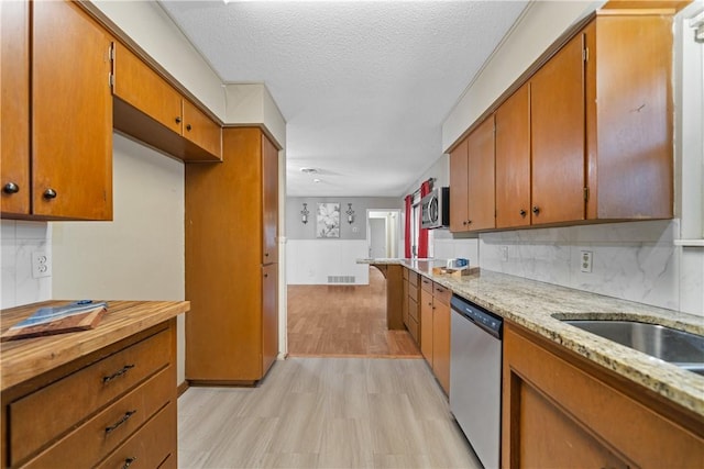 kitchen with light wood-type flooring, stainless steel appliances, a textured ceiling, and backsplash