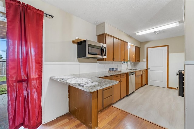 kitchen featuring decorative backsplash, sink, light wood-type flooring, stainless steel appliances, and a textured ceiling