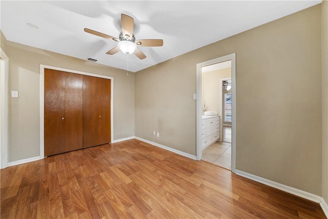 unfurnished bedroom featuring ceiling fan, a closet, connected bathroom, and light hardwood / wood-style flooring