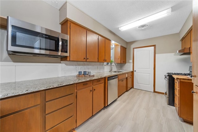 kitchen with a textured ceiling, appliances with stainless steel finishes, tasteful backsplash, sink, and light stone counters