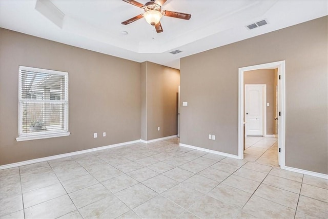 tiled empty room with ceiling fan and a raised ceiling