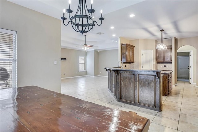 kitchen featuring sink, light tile patterned floors, a breakfast bar area, hanging light fixtures, and ceiling fan with notable chandelier