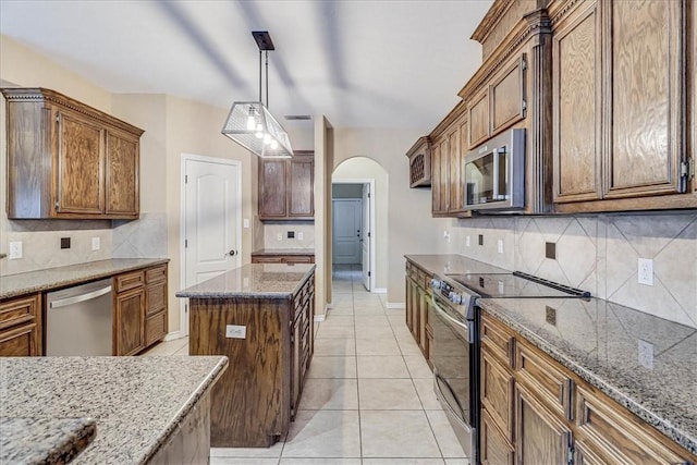 kitchen featuring tasteful backsplash, light tile patterned floors, appliances with stainless steel finishes, pendant lighting, and dark stone counters