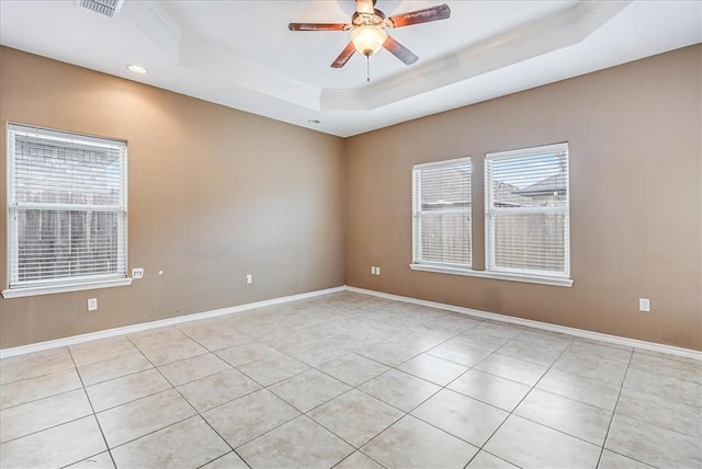 unfurnished room with a raised ceiling, a wealth of natural light, ceiling fan, and light tile patterned floors