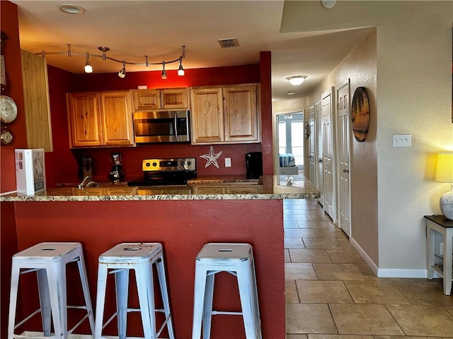 kitchen featuring light tile patterned floors, stainless steel appliances, a kitchen breakfast bar, and kitchen peninsula