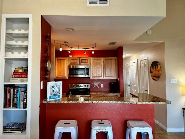 kitchen with stainless steel appliances, a kitchen breakfast bar, kitchen peninsula, and dark stone counters