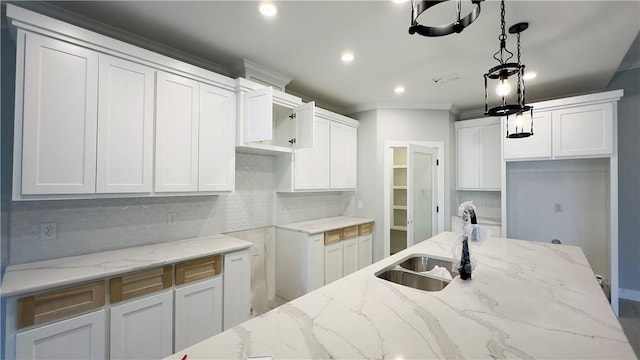 kitchen featuring a sink, decorative backsplash, light stone counters, and decorative light fixtures