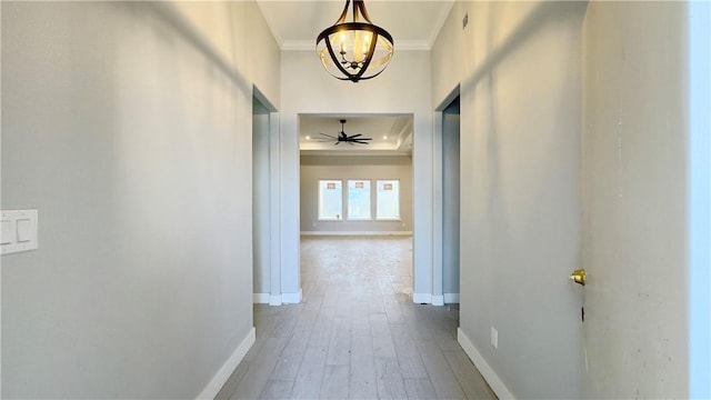 hall with wood finished floors, baseboards, an inviting chandelier, a tray ceiling, and ornamental molding