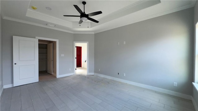 unfurnished bedroom featuring wood finished floors, baseboards, crown molding, a walk in closet, and a raised ceiling