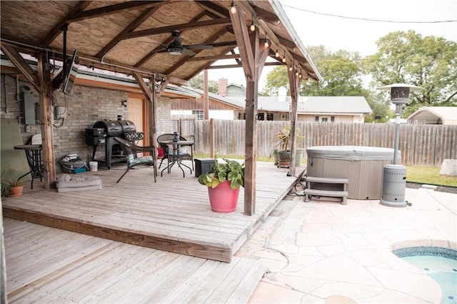 wooden terrace with a fenced backyard, a ceiling fan, a hot tub, and a patio