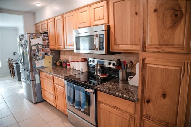 kitchen with stainless steel appliances, light brown cabinetry, dark stone counters, decorative backsplash, and light tile patterned floors
