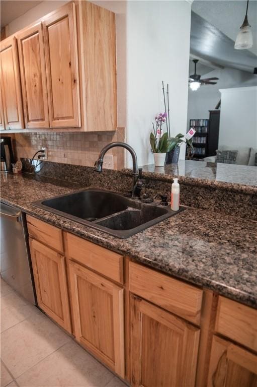 kitchen featuring stainless steel dishwasher, a ceiling fan, dark stone countertops, a sink, and light tile patterned flooring