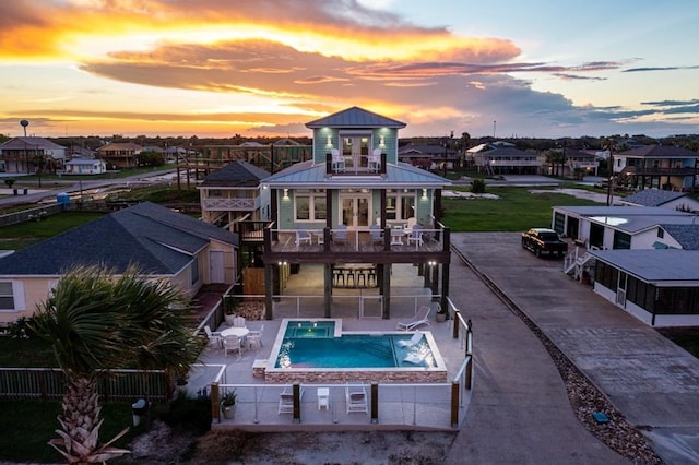 back house at dusk with a patio area, a balcony, and a swimming pool with hot tub